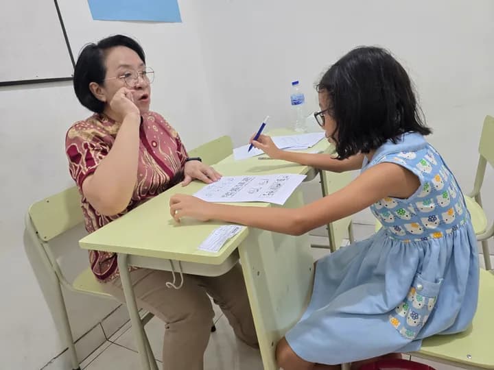 Psikolog duduk berhadapan dengan seorang anak yang sedang menulis