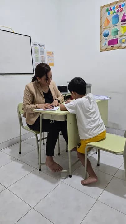 Seorang anak mengerjakan tugas di meja didampingi psikolog